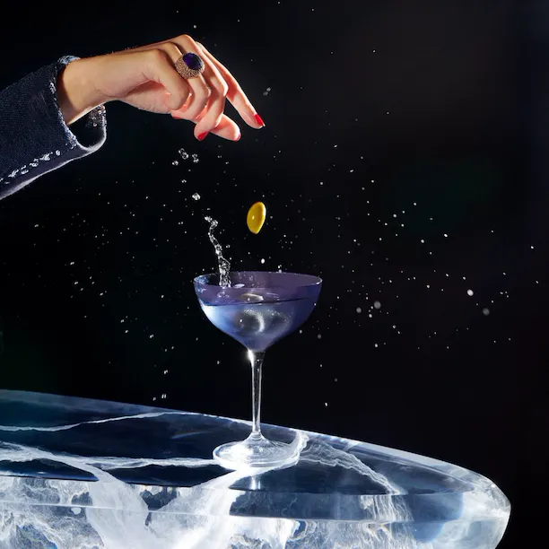 dry martini cocktail on a black backdrop with a hand dropping olives
