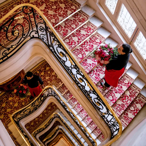 Hôtel Plaza Athénée, Paris, legendary red staircase with gold banister, and two florists holding red and pink bouquets.