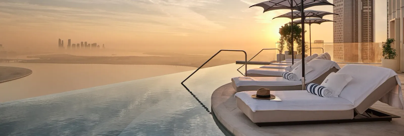 Sunloungers by The Lana's rooftop infinity pool at sunrise with view of Dubai