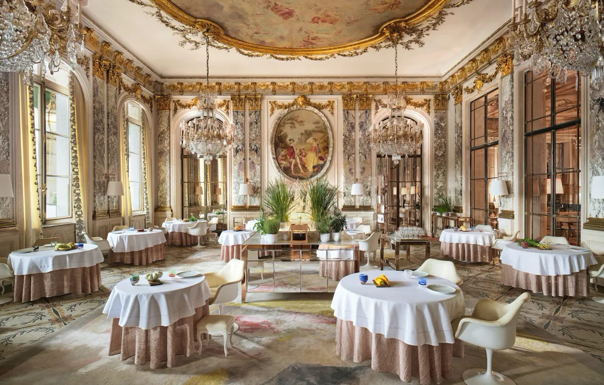Grande vue du Restaurant le Meurice Alain Ducasse avec les meubles, les lustres, les plantes et la nourriture sur les tables, au Meurice, Paris