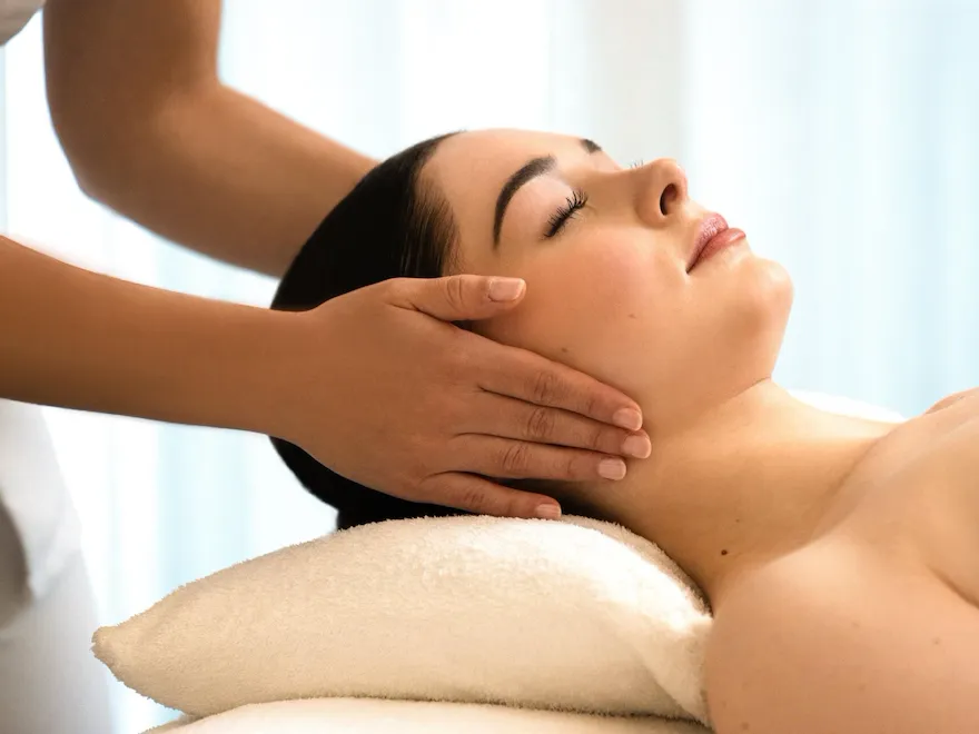 Nous pouvons voir une femme allongée sur une table de massage, reposant sa tête sur un oreiller blanc. Les mains de la masseuse sont placées sur les oreilles de la cliente. Les yeux du client sont fermés. Au spa Valmont au Meurice, à Paris.