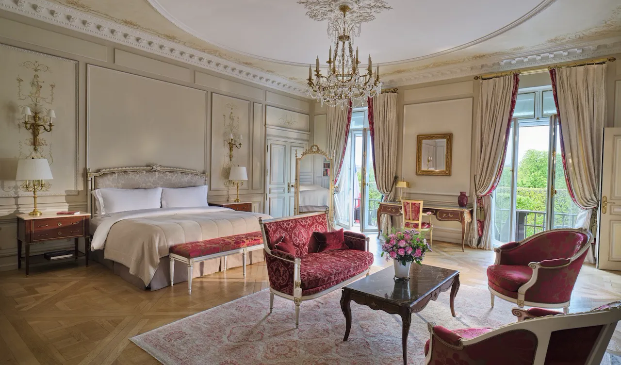 Large view of the Presidential Suite Dali with in first plan the furnitures of a living room like the couch, the rug and the chairs, and in the background the bed and the mirror, at Le Meurice, Paris