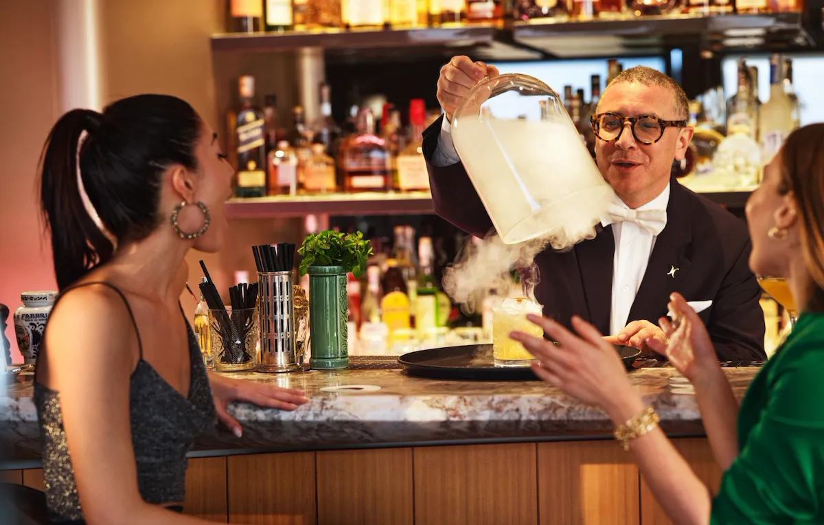 Barman serving spectacular cocktail at bar counter to two ladis at Il Giardino Bar