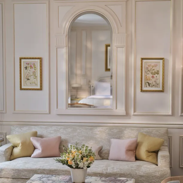 Livingroom area of a Deluxe Junior Suite with the table made with stone marquetry, the pillows on the couch and the mirror which reflect the bed, at Le Meurice, Paris