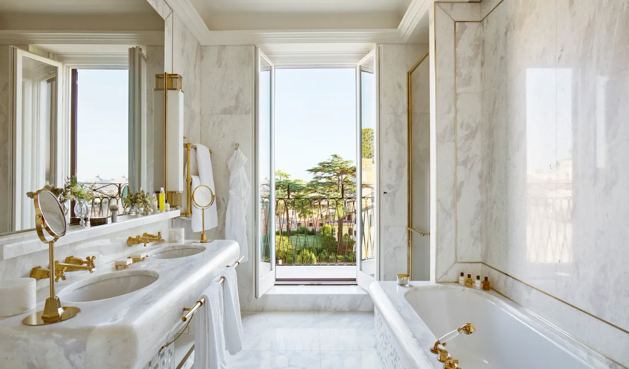 White marble bathroom of Presidential Suite with double sinks, bathtub and window with view of Rome at Hotel Eden
