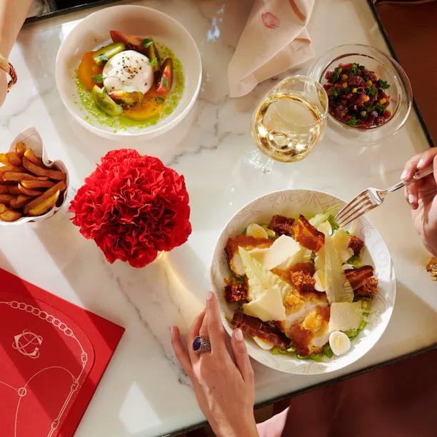 Women having lunch at La Galerie, view from their hands picking fries and eating a ceasar salad, McCarthy Salad and white wine on the table, at Hotel Plaza Athénée, Paris
