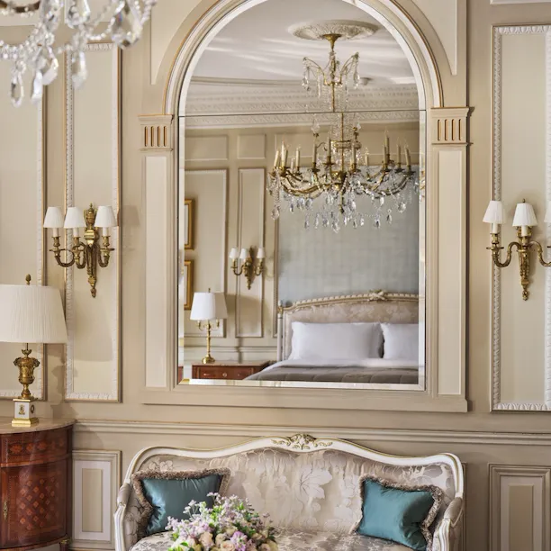 View on the table made with stone marquetry and a couch with a mirror above, which reflects the chandelier and the bed, at Le Meurice, Paris