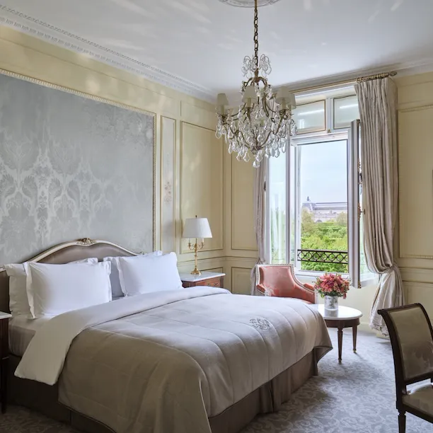 Heritage Suite view from the right side of the bed, next to a chair and a table with flower on the top, in front of the window, at Le Meurice, Paris