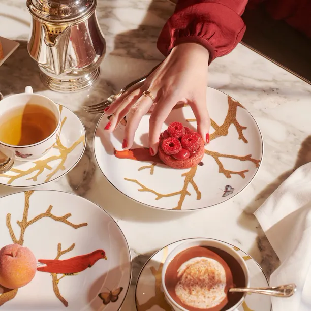 Some details of the tea time with a hand taking a raspberry cookie of Cédric Grolet next to hot drinks and a peach, at Le Meurice, Paris