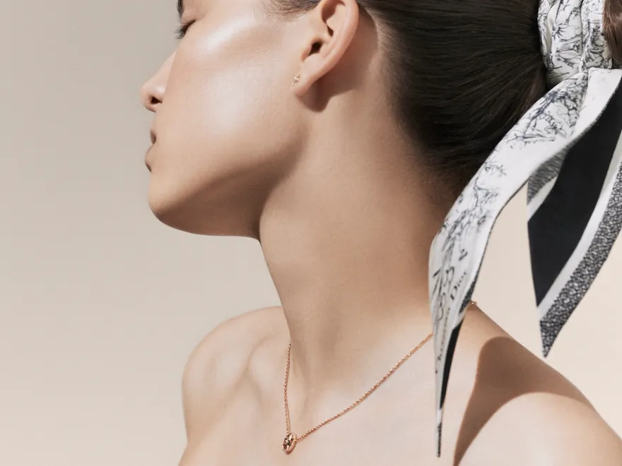 Dior Spa Plaza Athénée's iconography for spa treatments. Here, a light-skin female model posing with her head leaning towards her right side, accessorised with a toile de jouy head band and a short pink gold necklace.