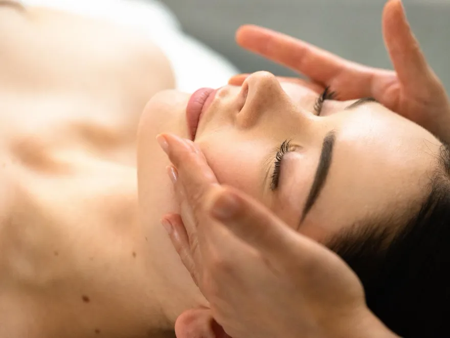 We can see the masseuse's two hands on the client’s cheeks. Her eyes are closed. We can see a focus on the client’s face at Le Meurice, Paris.